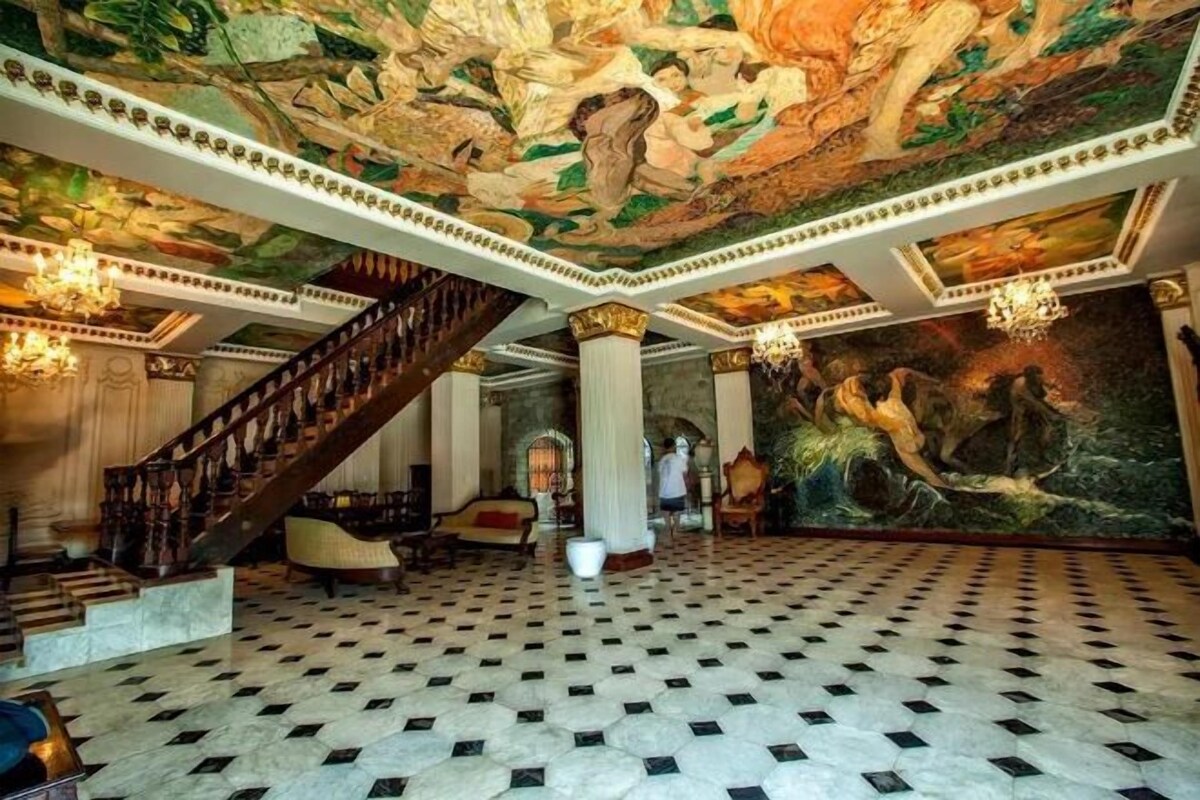Un vaste hall d’entrée avec un sol à carreaux, un escalier et une grande fresque murale.