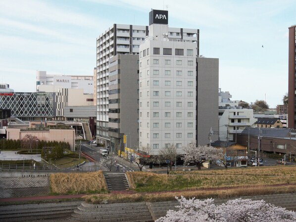 A multi-story building with a prominent APA sign on top, surrounded by other buildings and a park with cherry blossoms. - APA Hotel Mito-ekimae (Mito)