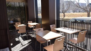 An outdoor seating area with tables and chairs, a patterned floor, and a view of the street and buildings. - APA Hotel Mito-ekimae (Mito)
