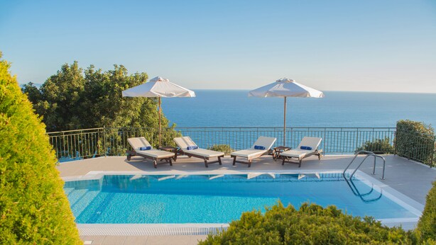 A pool with lounge chairs and umbrellas, overlooking the sea.
