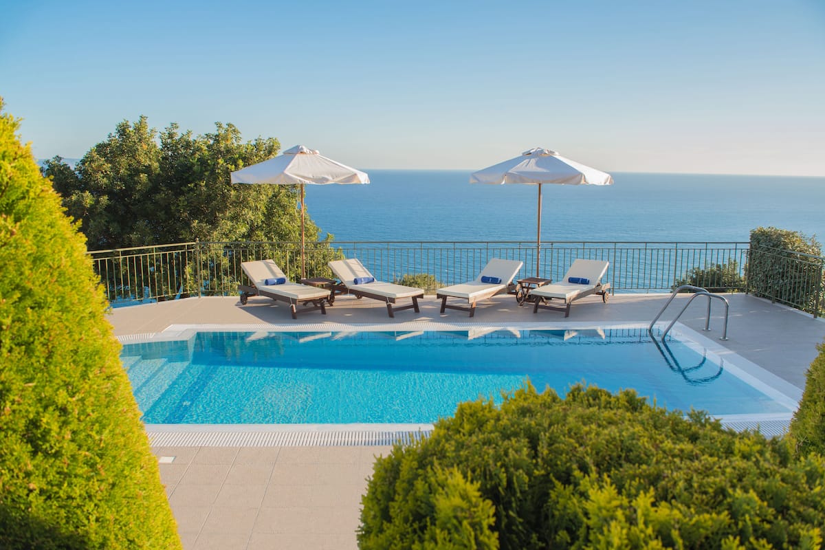 A pool with lounge chairs and umbrellas, overlooking the sea.