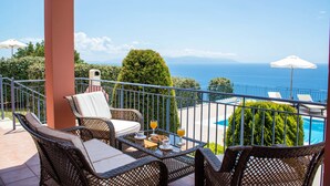 A balcony with wicker furniture, a table with drinks, and a view of the sea.
