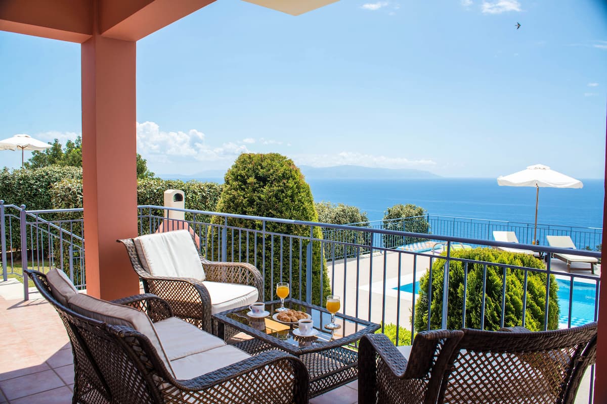 A balcony with wicker furniture, a table with drinks, and a view of the sea.