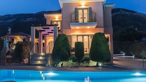 A two-story house with a balcony, a swimming pool, and a mountain backdrop.