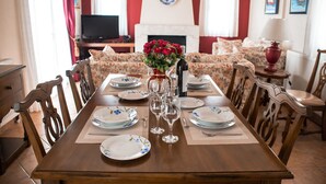 A dining table set for four with floral-patterned chairs, a vase of red flowers, and a fireplace in the background.