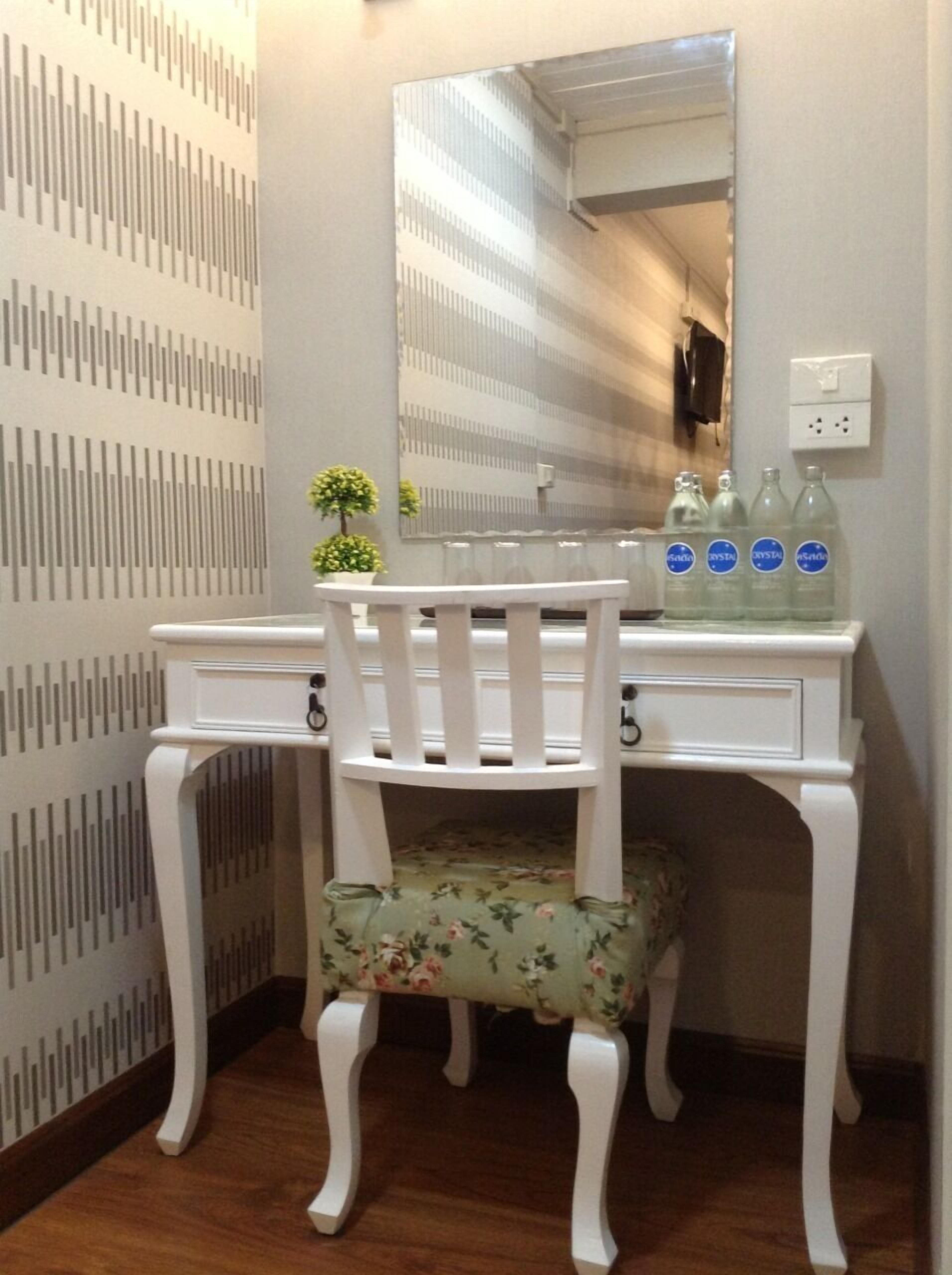 A white vanity with a mirror, a small potted plant, and three bottles of water on the counter.