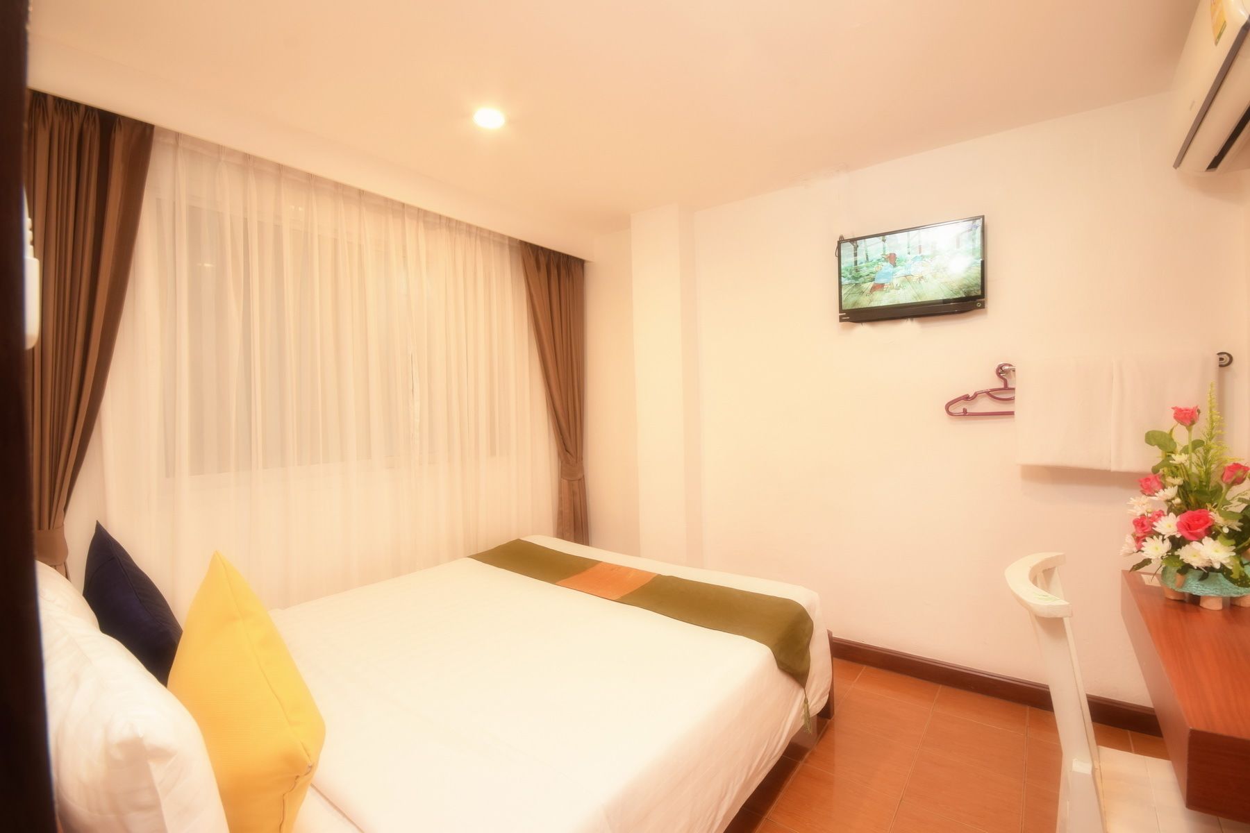 A hotel room with a bed, a television mounted on the wall, a small sink, and a potted plant.