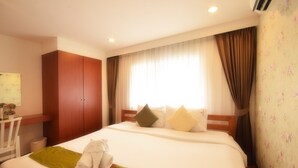 Une chambre d’hôtel avec un lit, une armoire en bois, un bureau avec une chaise et une fenêtre avec des rideaux.