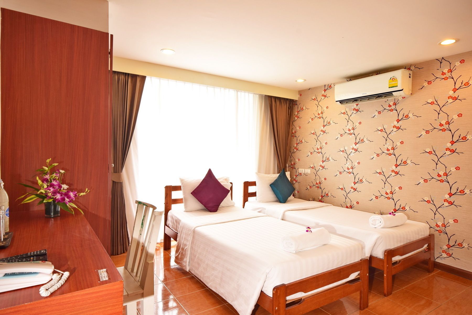 A hotel room with two single beds, a desk with a telephone, and a window with curtains.