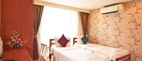 A hotel room with two single beds, a desk with a telephone, and a window with curtains.