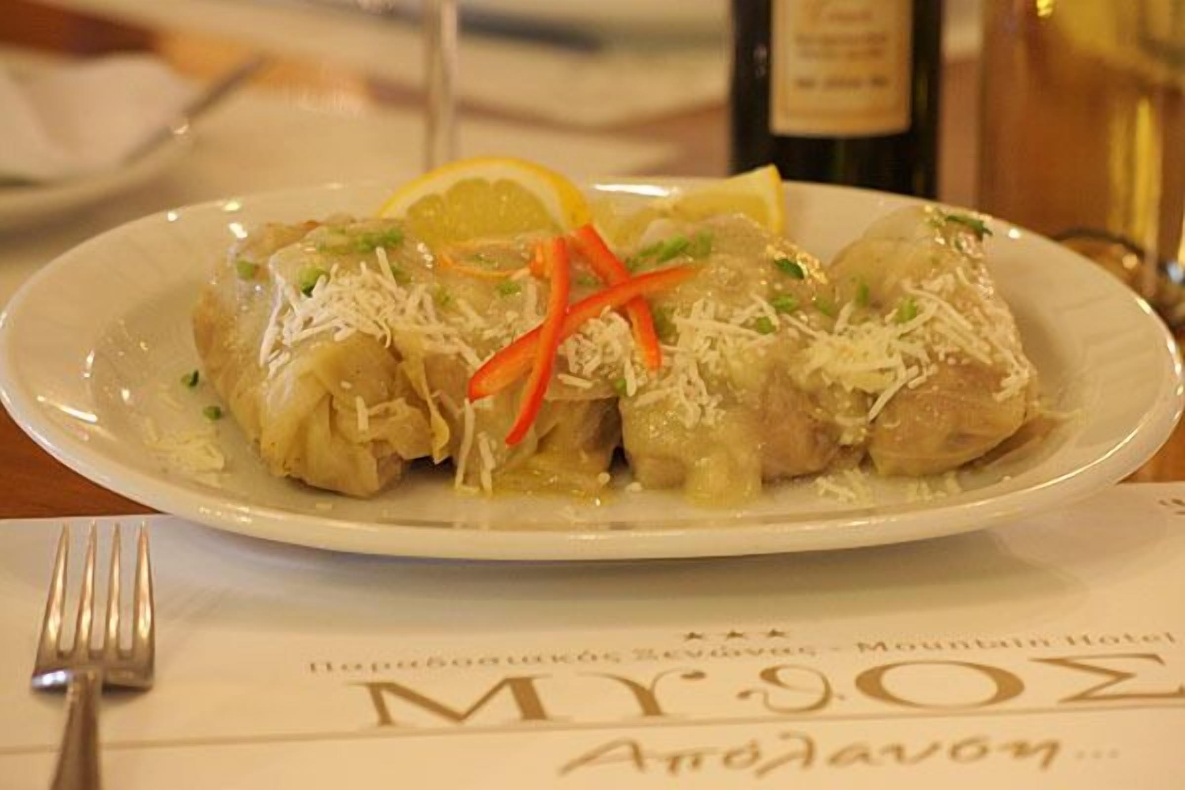 Un plato de rollos de repollo rellenos, adornados con queso rallado y rodajas de limón, servido en un plato blanco.
