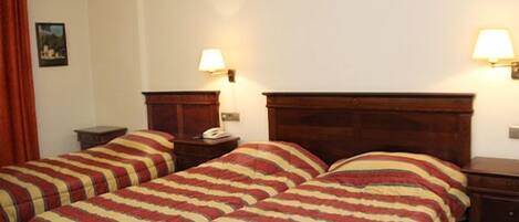 Una habitación con dos camas, cada una con ropa de cama a rayas, cabeceros de madera, mesitas de noche con lámparas y un cuadro en la pared.