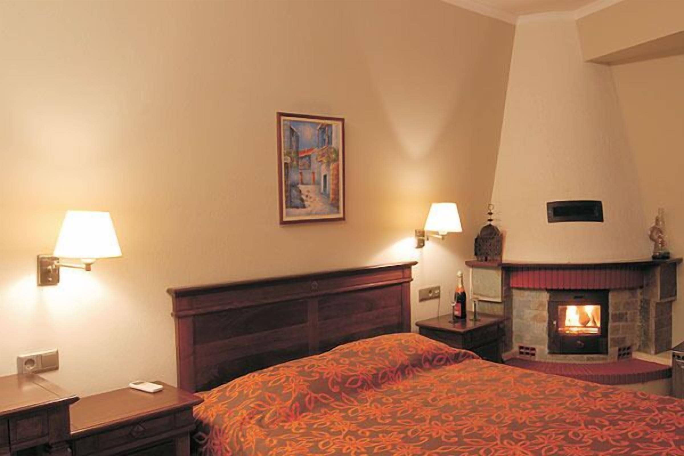 Quarto de hotel com cama, mesa de cabeceira, luminária na parede, quadro e lareira.
