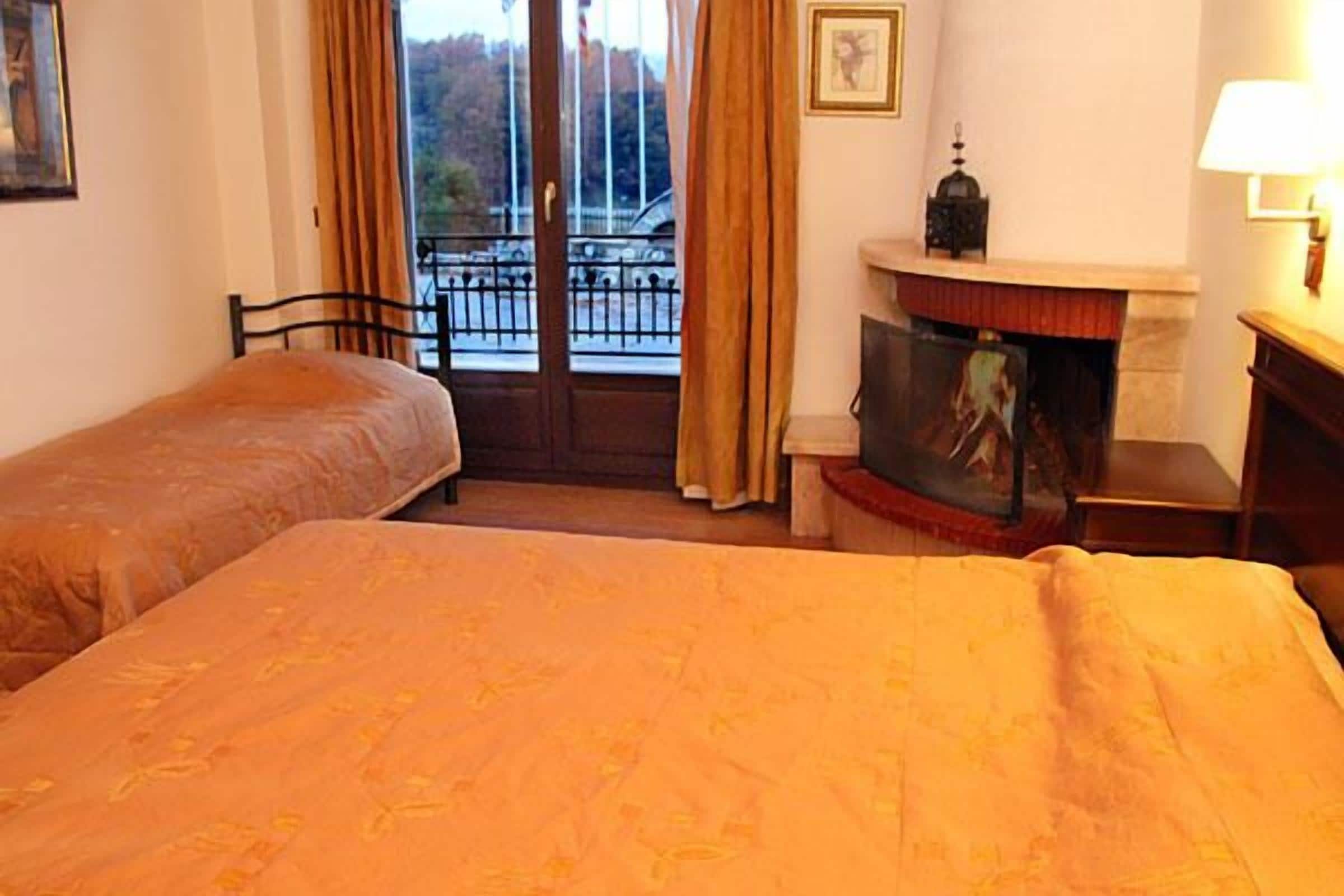 A hotel room with two beds, a fireplace, a television, and a balcony with a view of the outside.