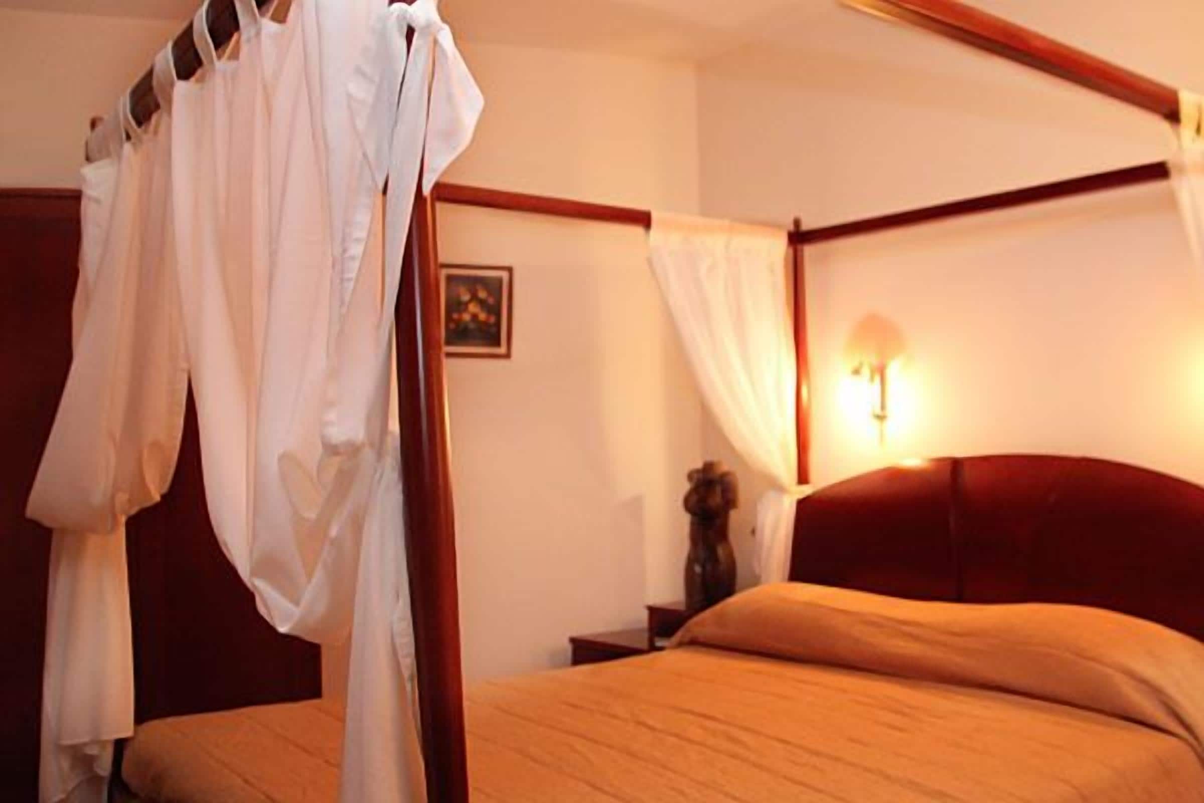 A four-poster bed with a canopy, a bedside table with a lamp, and a framed picture on the wall.