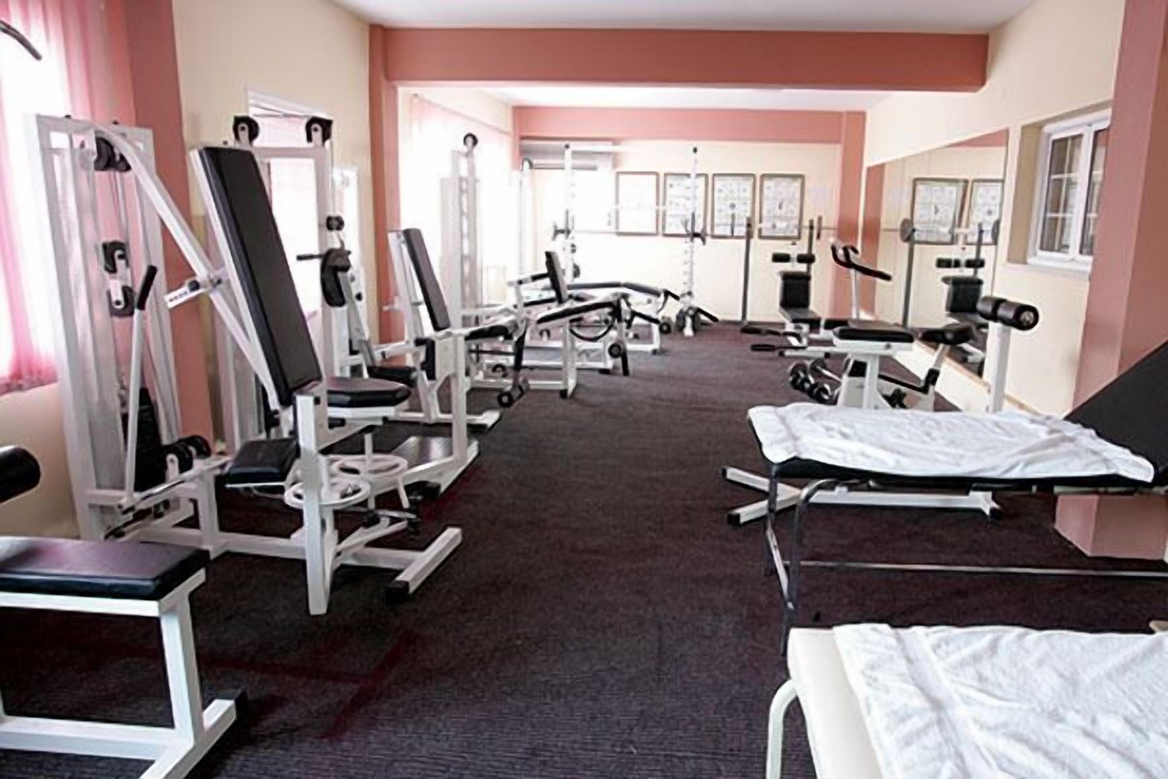 Un gimnasio con diferentes máquinas de ejercicio, suelo alfombrado y una pared con cuadros enmarcados.