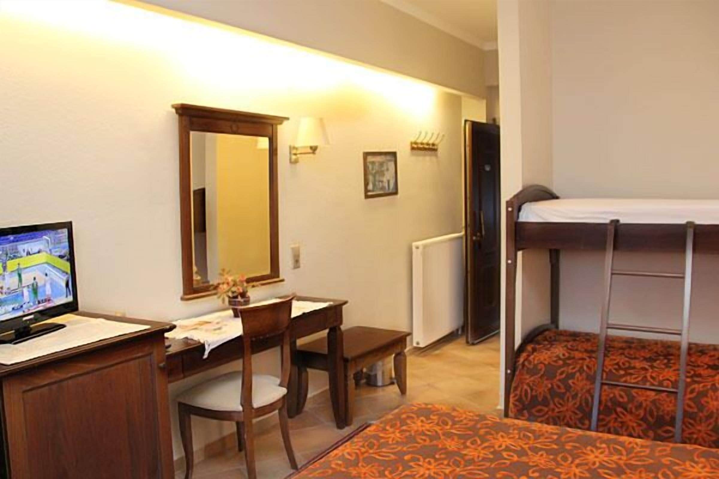 A hotel room with a bunk bed, a desk with a chair, a television, a mirror, and a radiator.