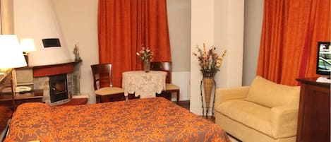 A hotel room with a large bed, a sofa, a small table with a vase of flowers, a fireplace, and a television.