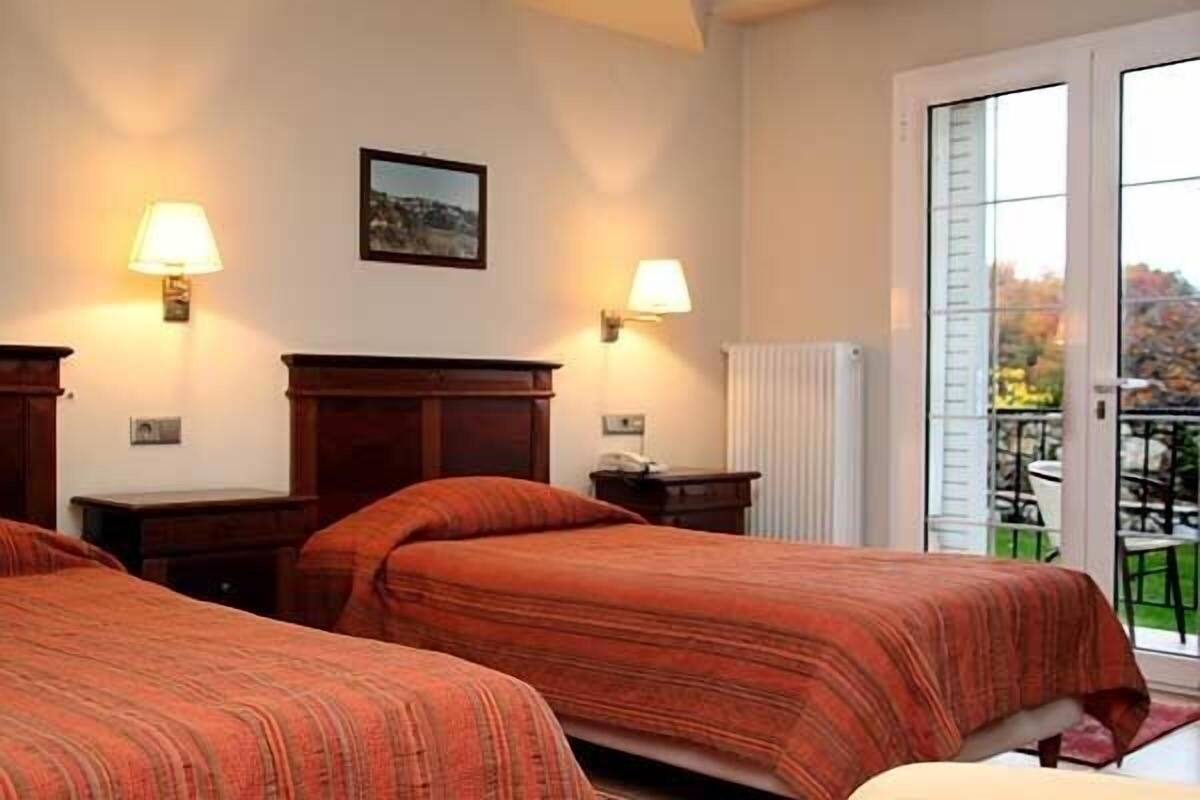 Et hotelværelse med to senge, to sengeborde, to væglamper, en radiator og en skydedør til et udendørs område.