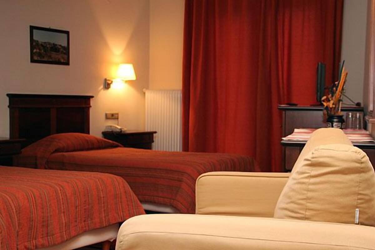 Et hotelværelse med to senge, en sofa, en lampe, en radiator og et billede på væggen.
