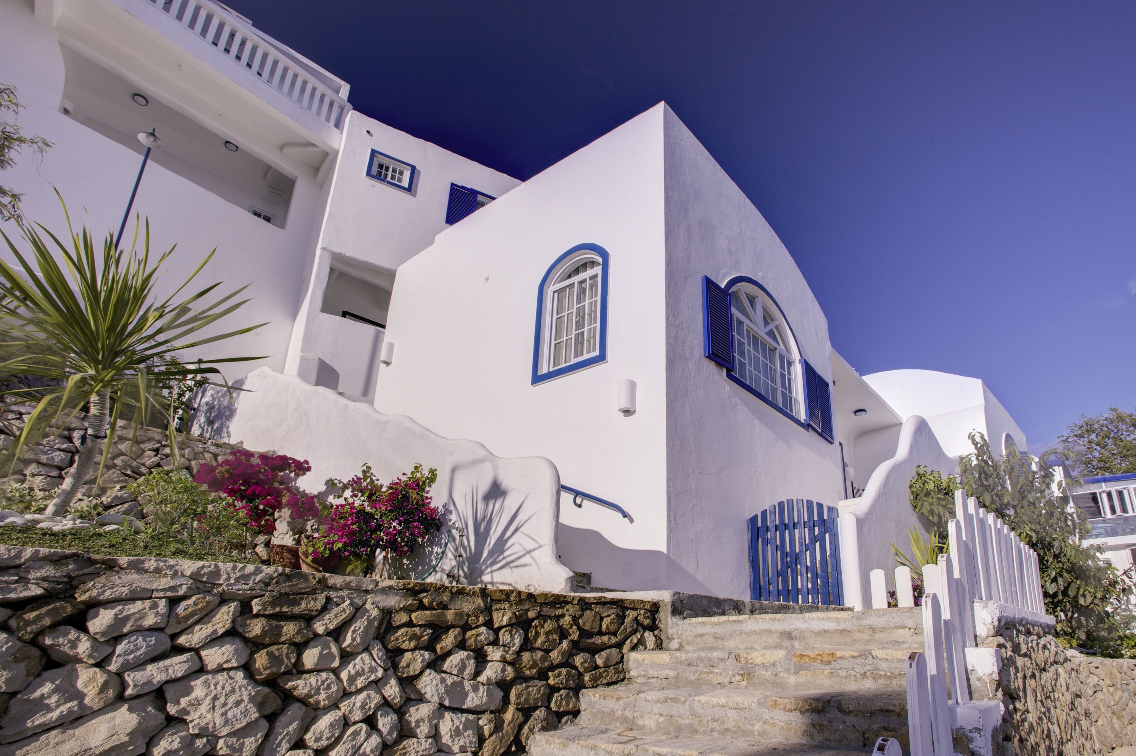 A white building with blue accents, stone steps, and a stone wall.