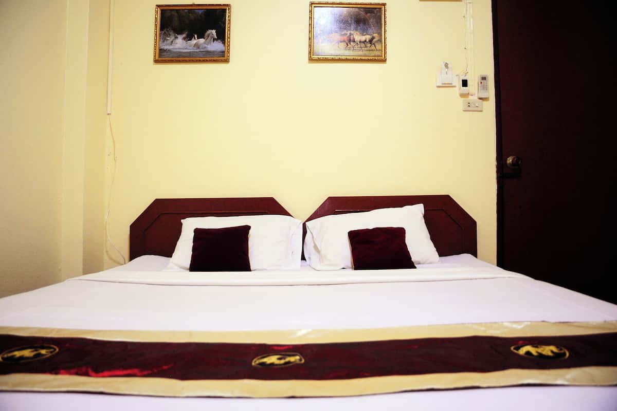 Quarto de hotel com uma cama, duas fotos emolduradas na parede e uma porta.