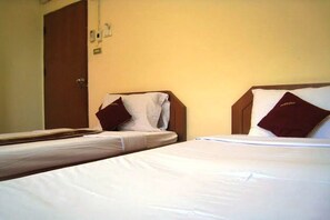 Two single beds with white linens and maroon pillows, a wooden headboard, and a closed door in a room with beige walls.
