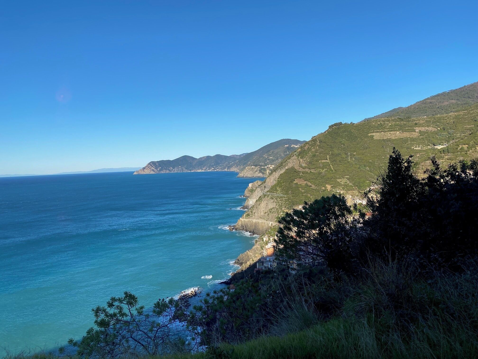 Eine Küstenlandschaft mit freiem Blick auf das Meer und eine Hügelkuppe mit Gebäuden.