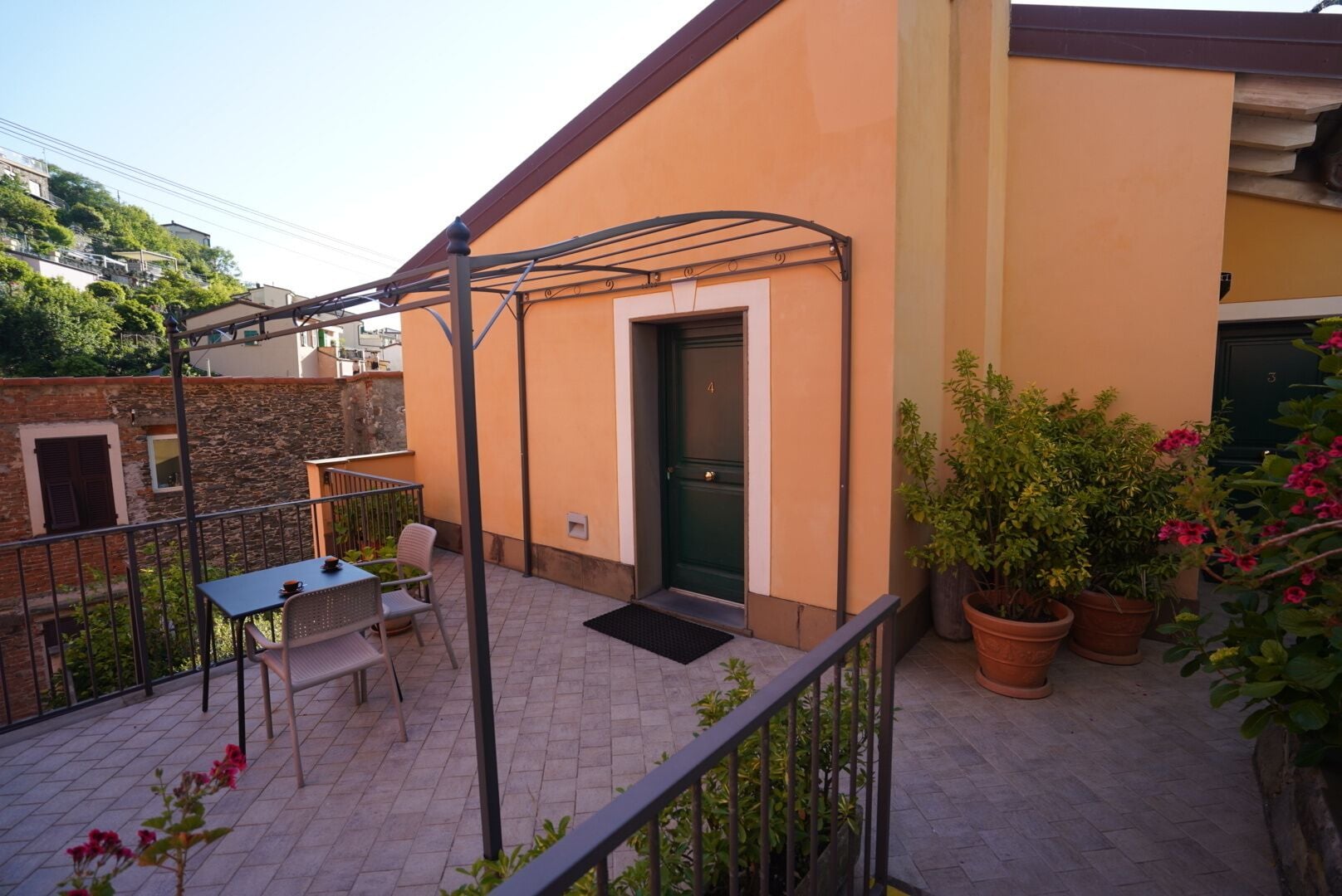 A balcony with a table and chairs, a green door, and potted plants.