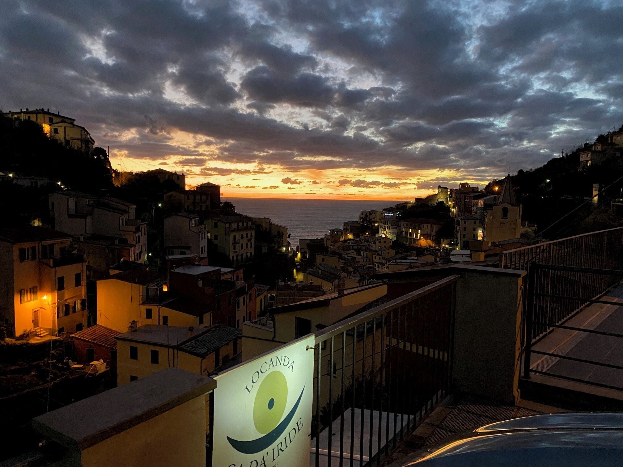 A coastal town at sunset with buildings and a sign for Locanda da'Iride.