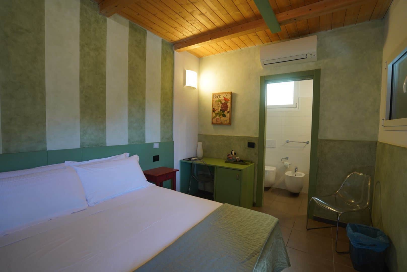 Habitació amb un llit, un escriptori petit, un mirall, un lavabo i un vàter.