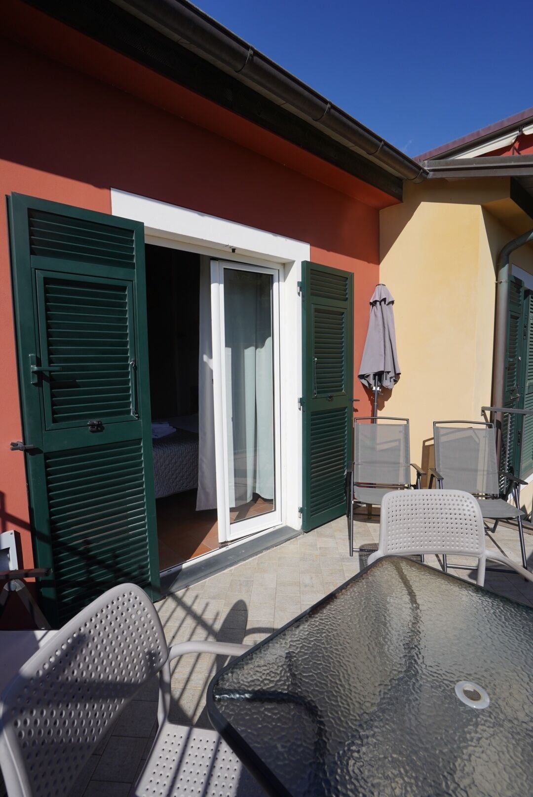 An outdoor patio with a glass table, two chairs, and a sliding glass door leading to a room.