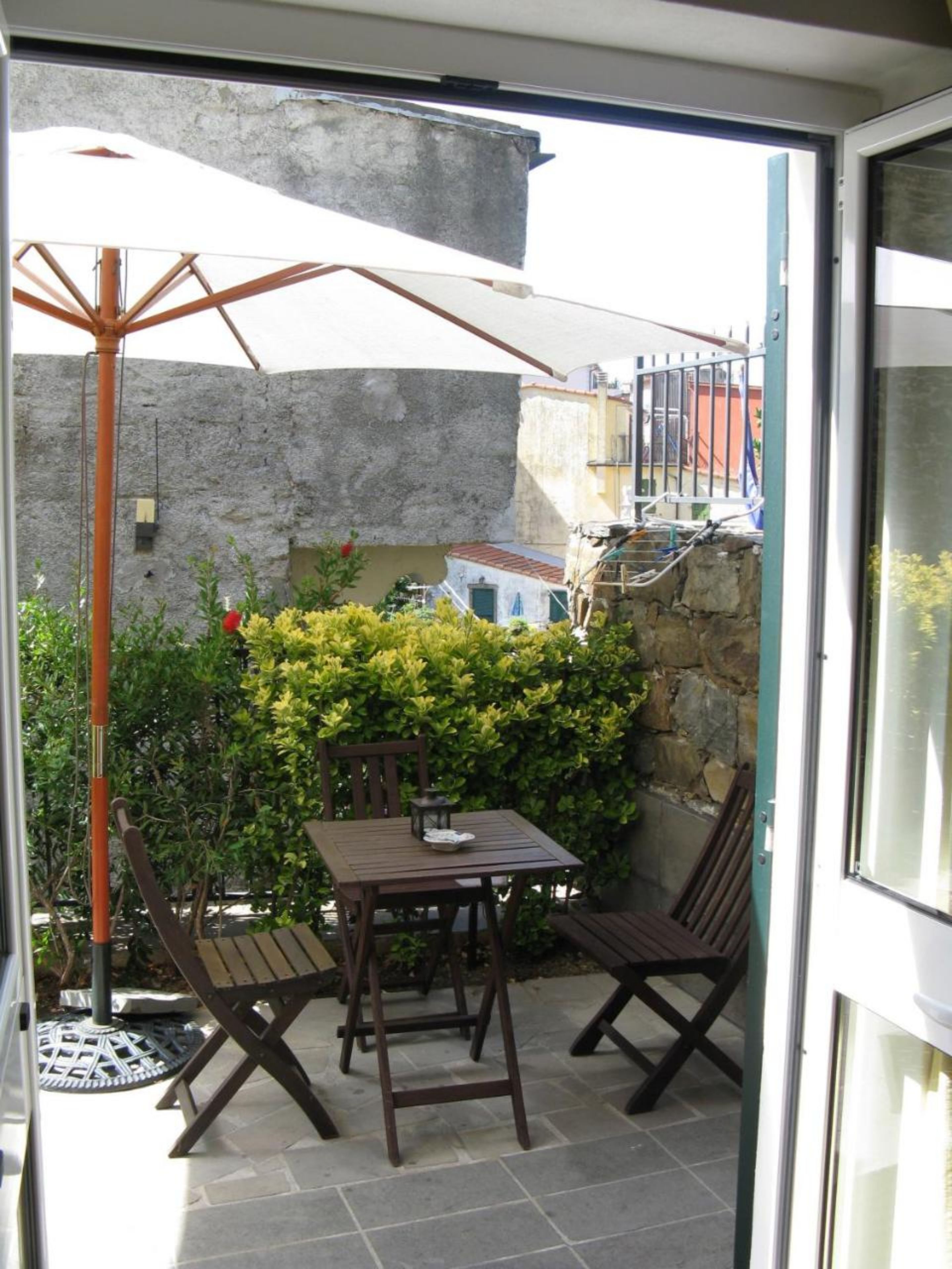 A patio with a table and two chairs, a metal umbrella, and a stone wall.