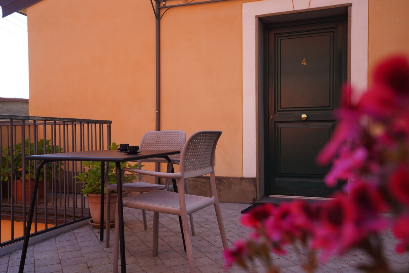 An outdoor seating area with a table and two chairs, a green door, and potted plants.