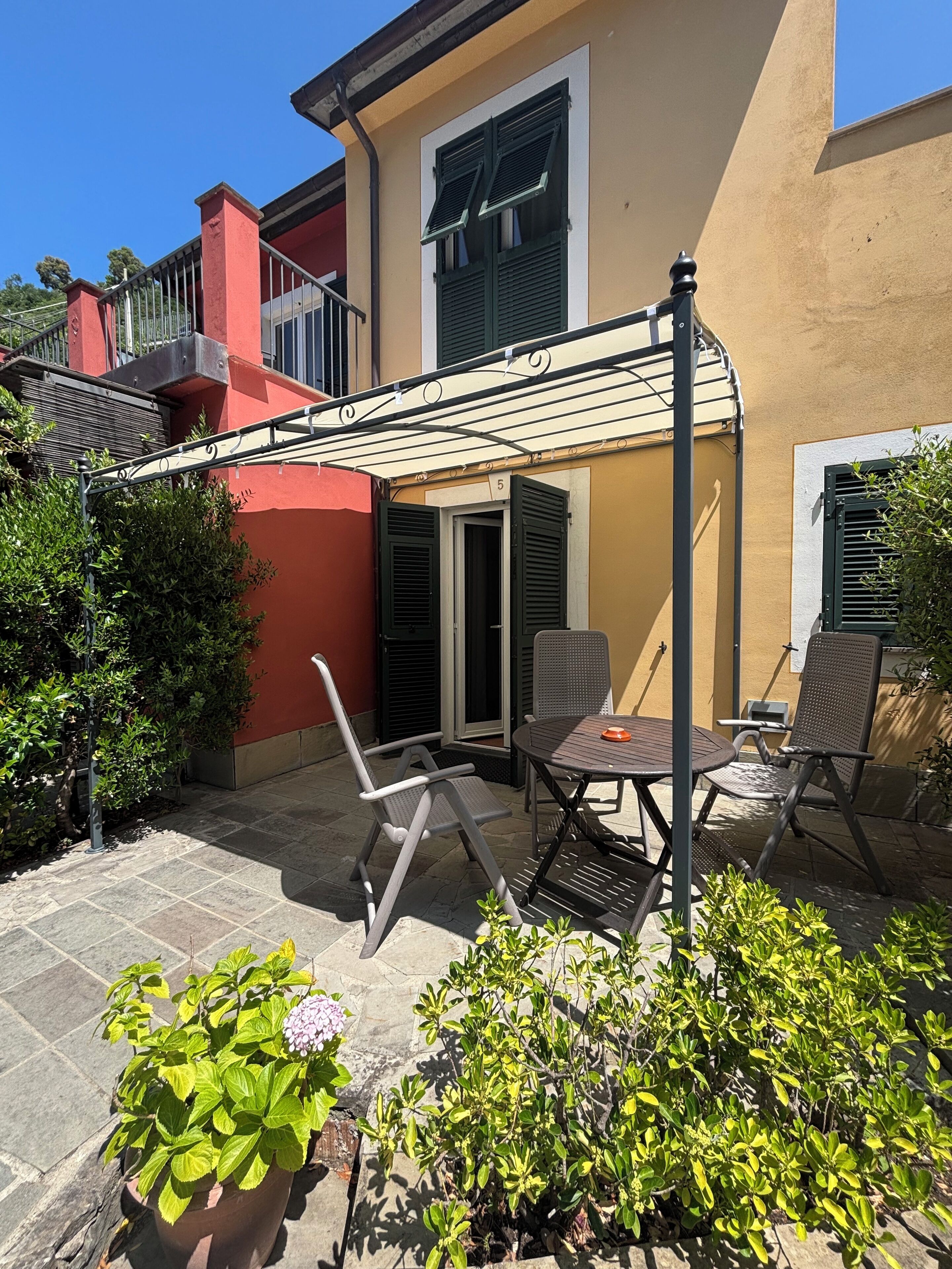 Un patio con mesa y sillas, una zona de estar cubierta y plantas en macetas.