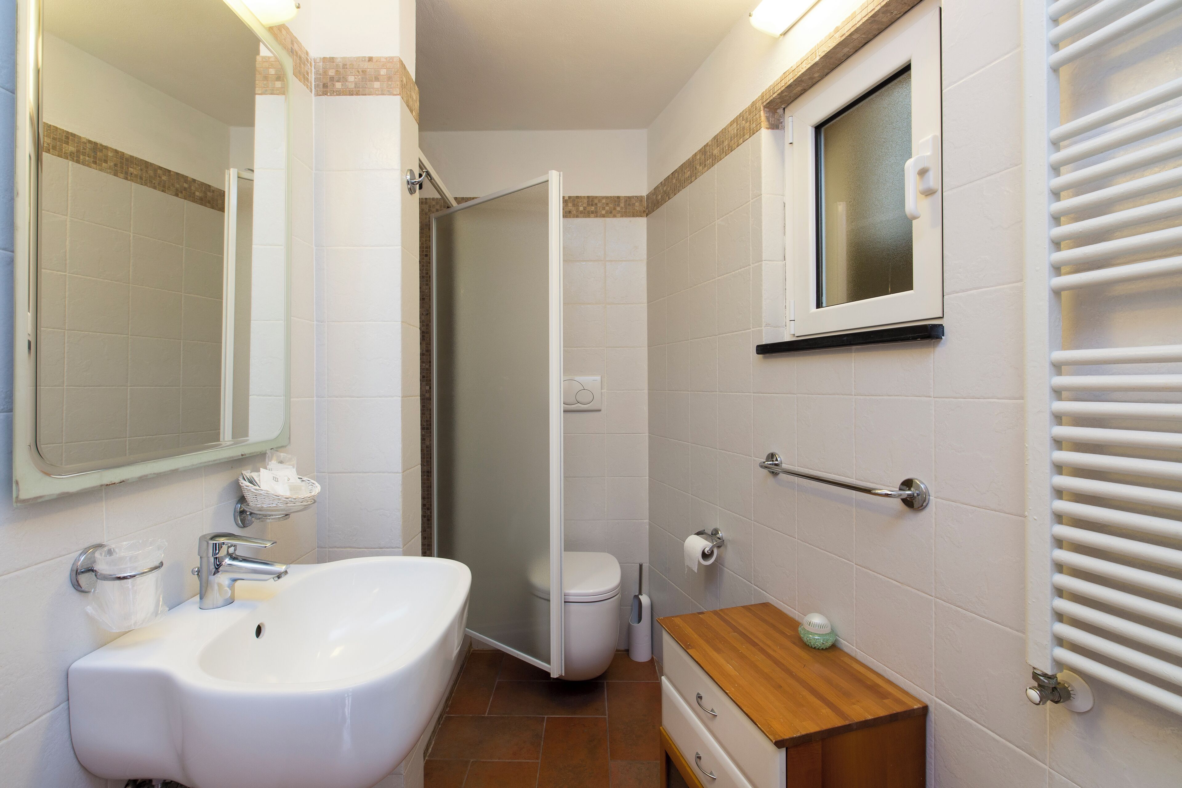 Un baño con lavamanos blanco, un espejo, ducha, inodoro y toallero.