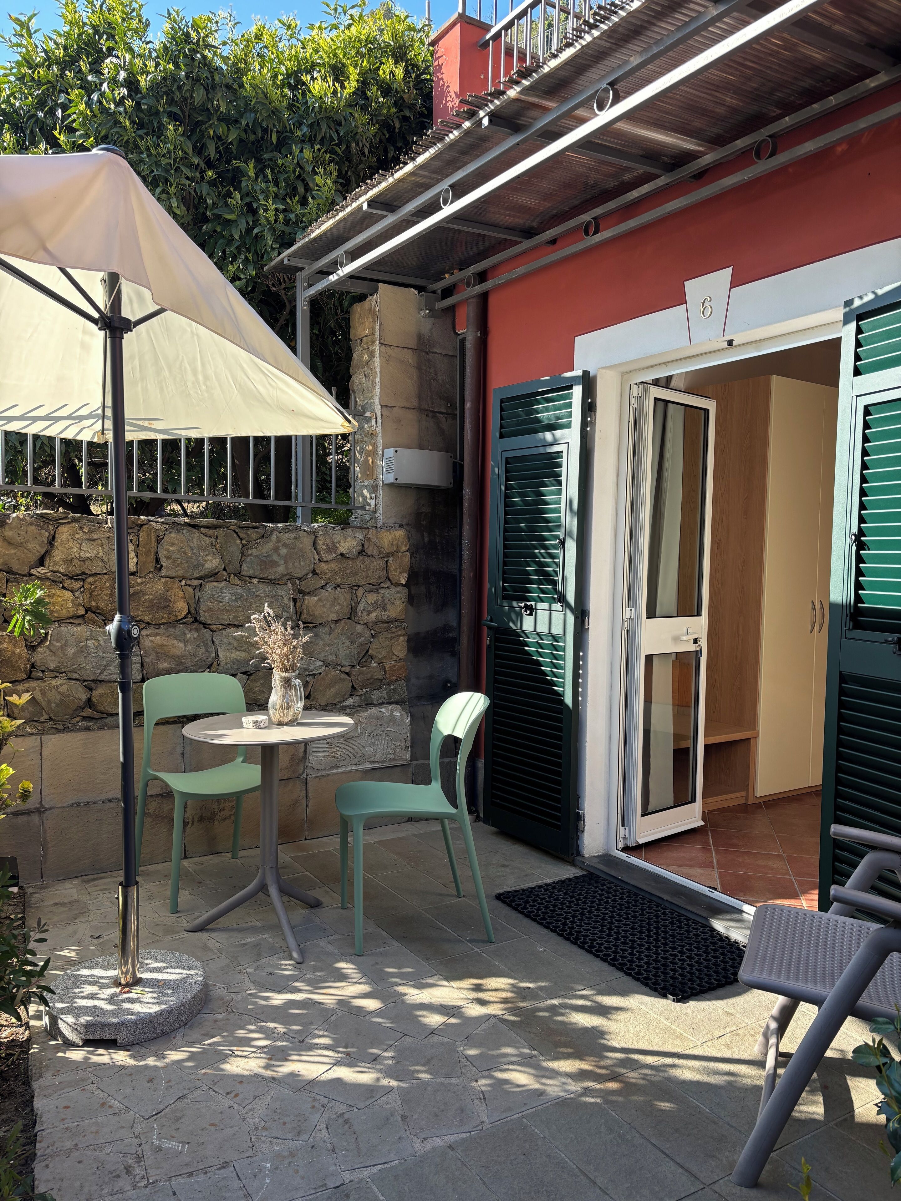A patio area with a table and chairs, a stone wall, and a door leading to a room.