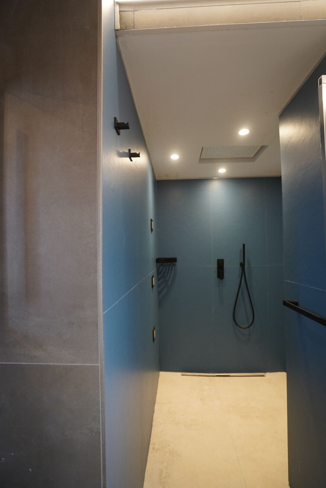A narrow, enclosed bathroom with blue walls, a shower area, and a toilet.