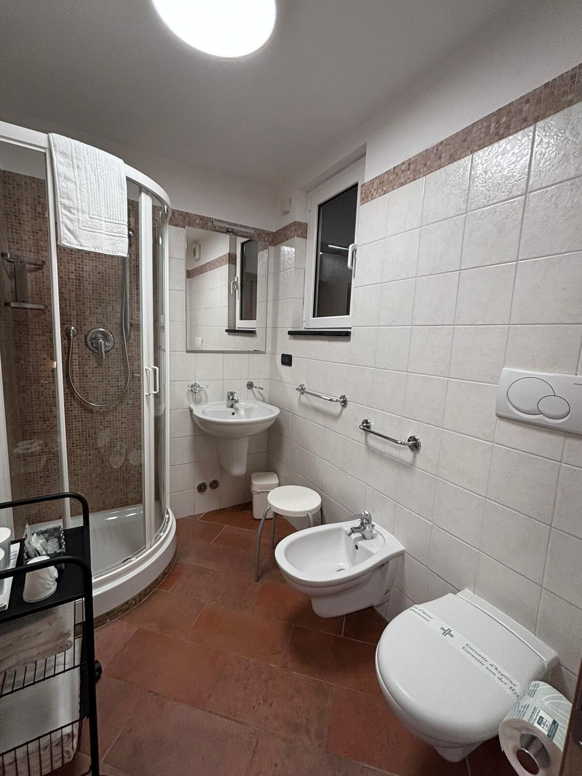A bathroom with a shower, two sinks, a toilet, and a bidet.