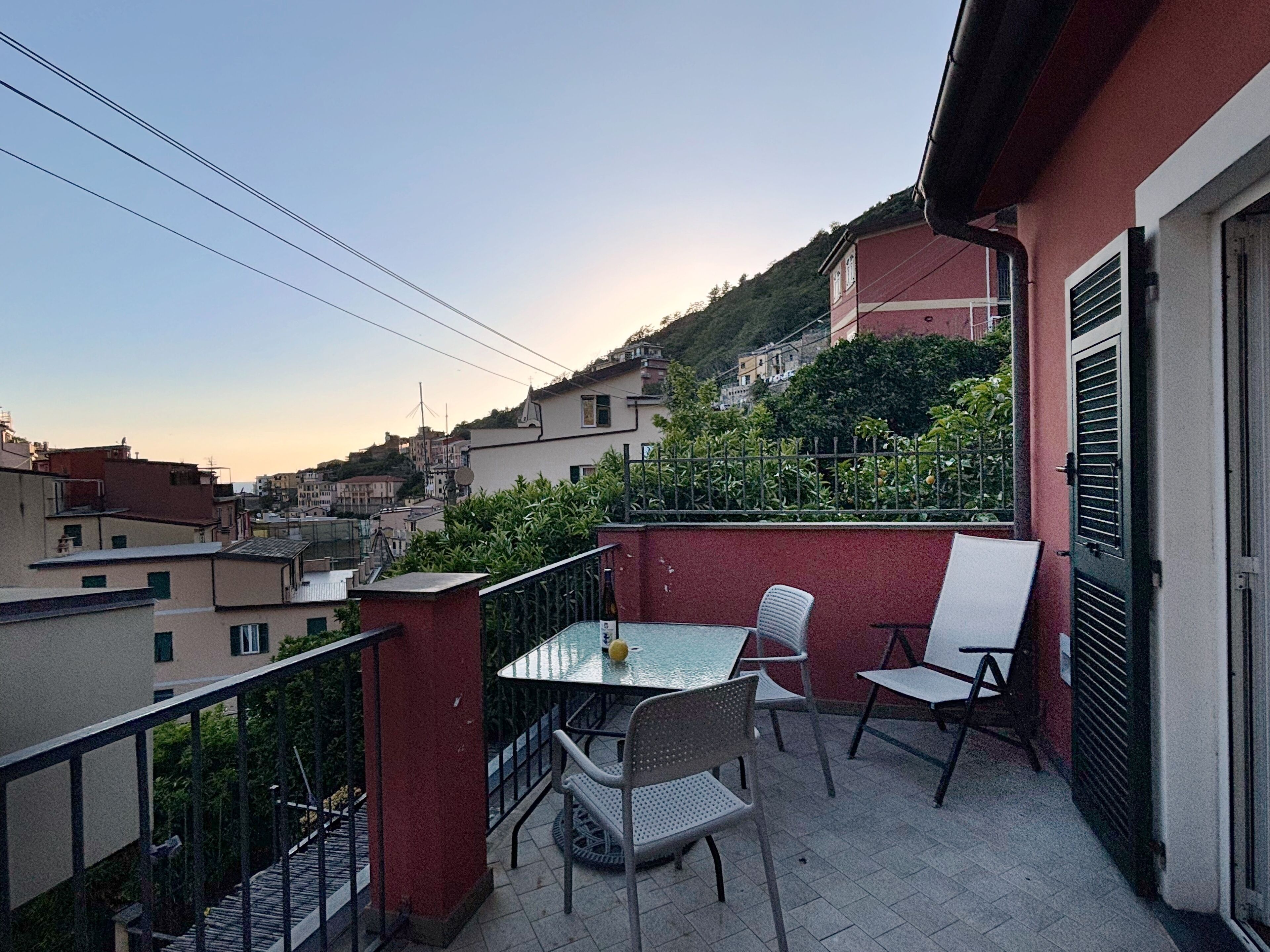 A balcony with a table and chairs, overlooking a hillside with buildings.