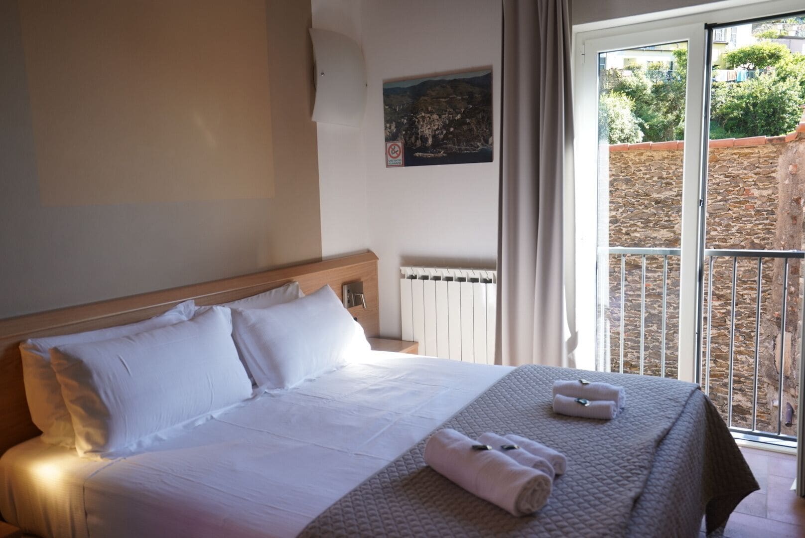 A hotel room with a bed, a view of a garden through a glass door, and a painting on the wall.