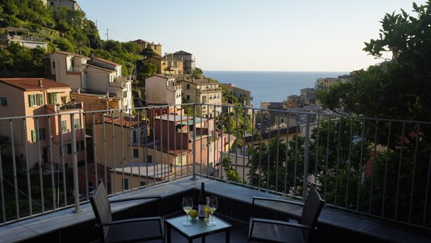 A balcony with two chairs and a table, overlooking a coastal town with buildings and the sea. - Locanda Ca Da Iride (Riomaggiore)