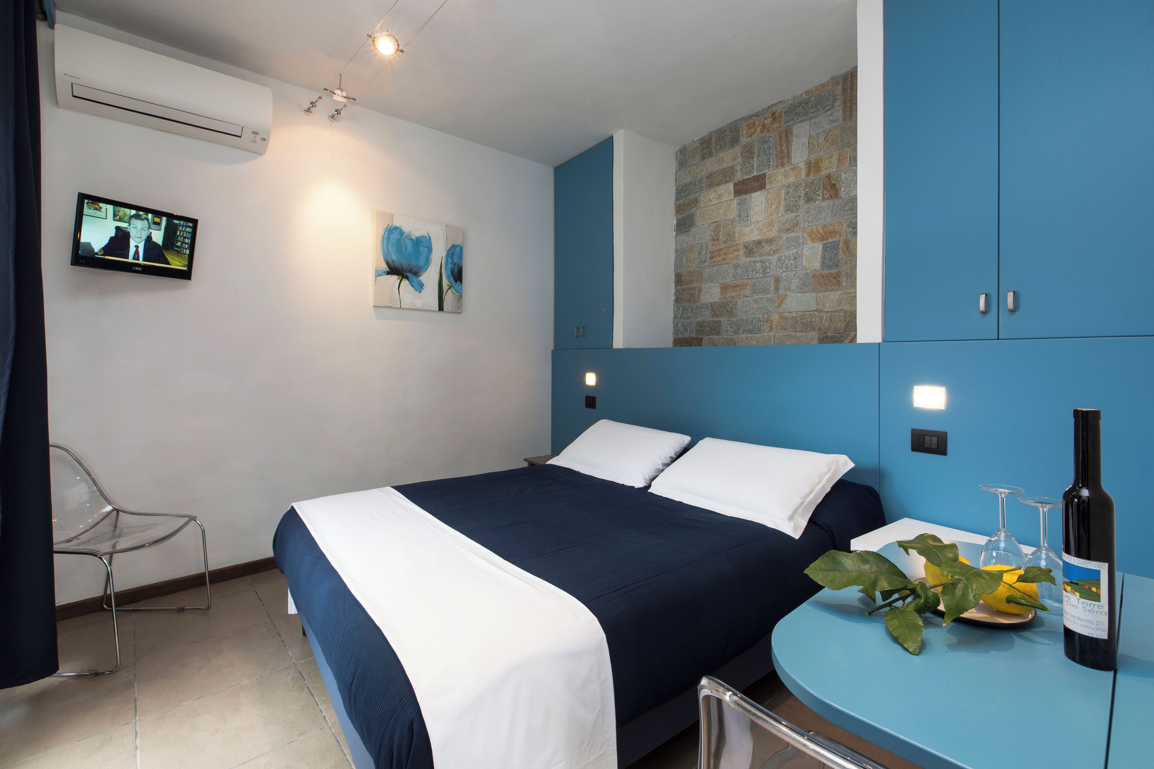 A modern hotel room with a large bed, a TV mounted on the wall, and a stone accent wall.