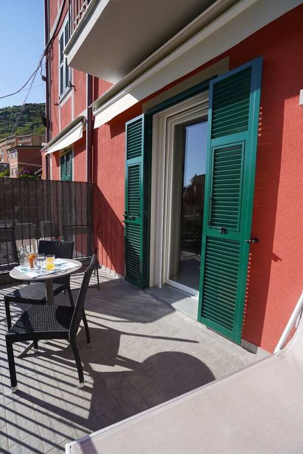 A red building with green shutters, a table with chairs, and a glass door. - Locanda Ca Da Iride (Riomaggiore)
