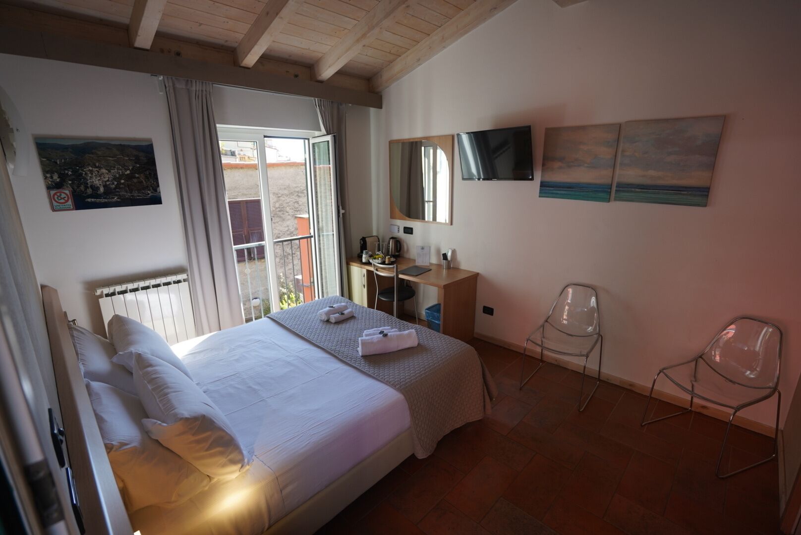 A bedroom with a bed, a desk, a chair, a television, and artwork on the walls.