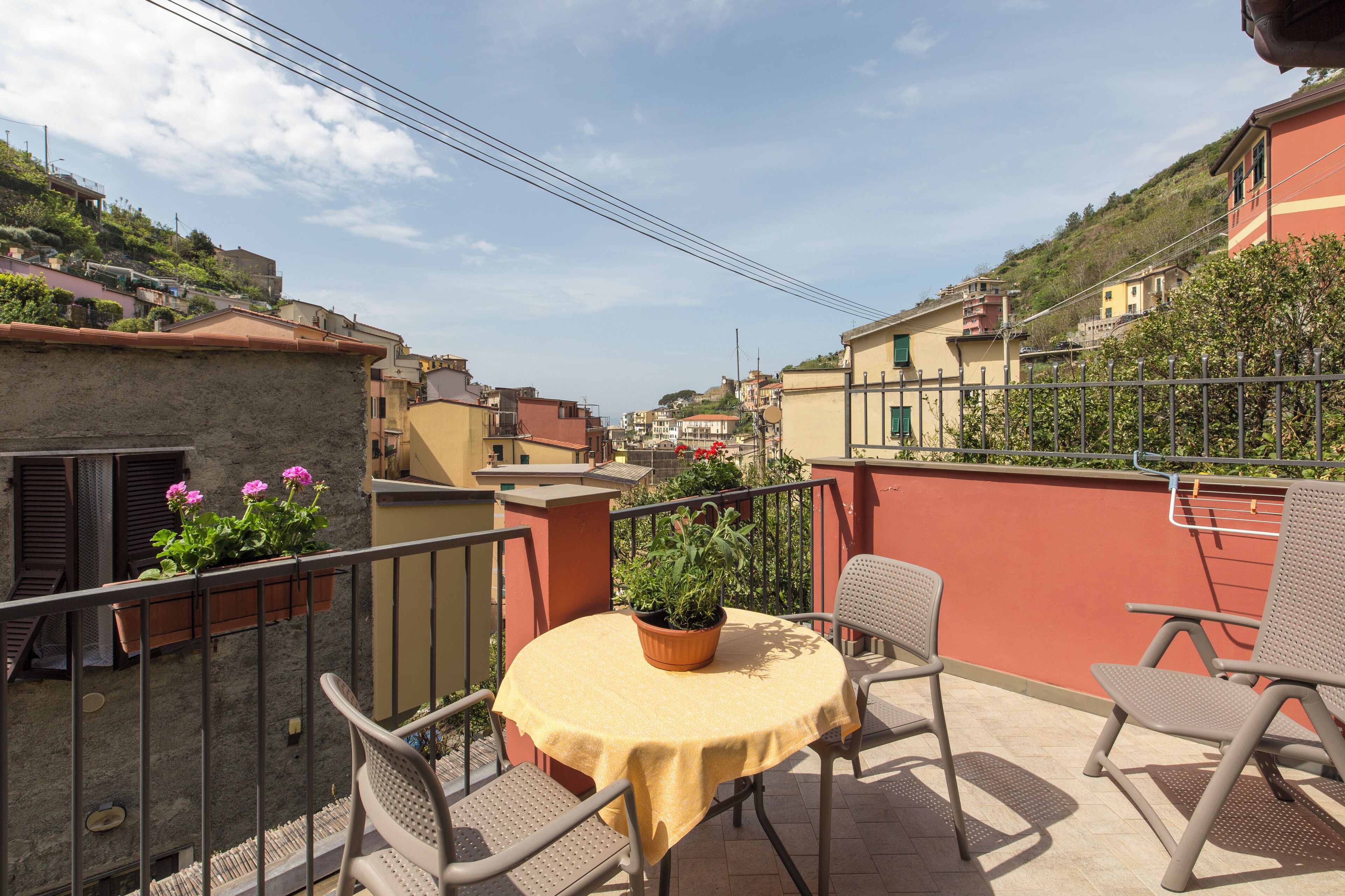A balcony with a round table and two chairs, overlooking a hillside residential area.