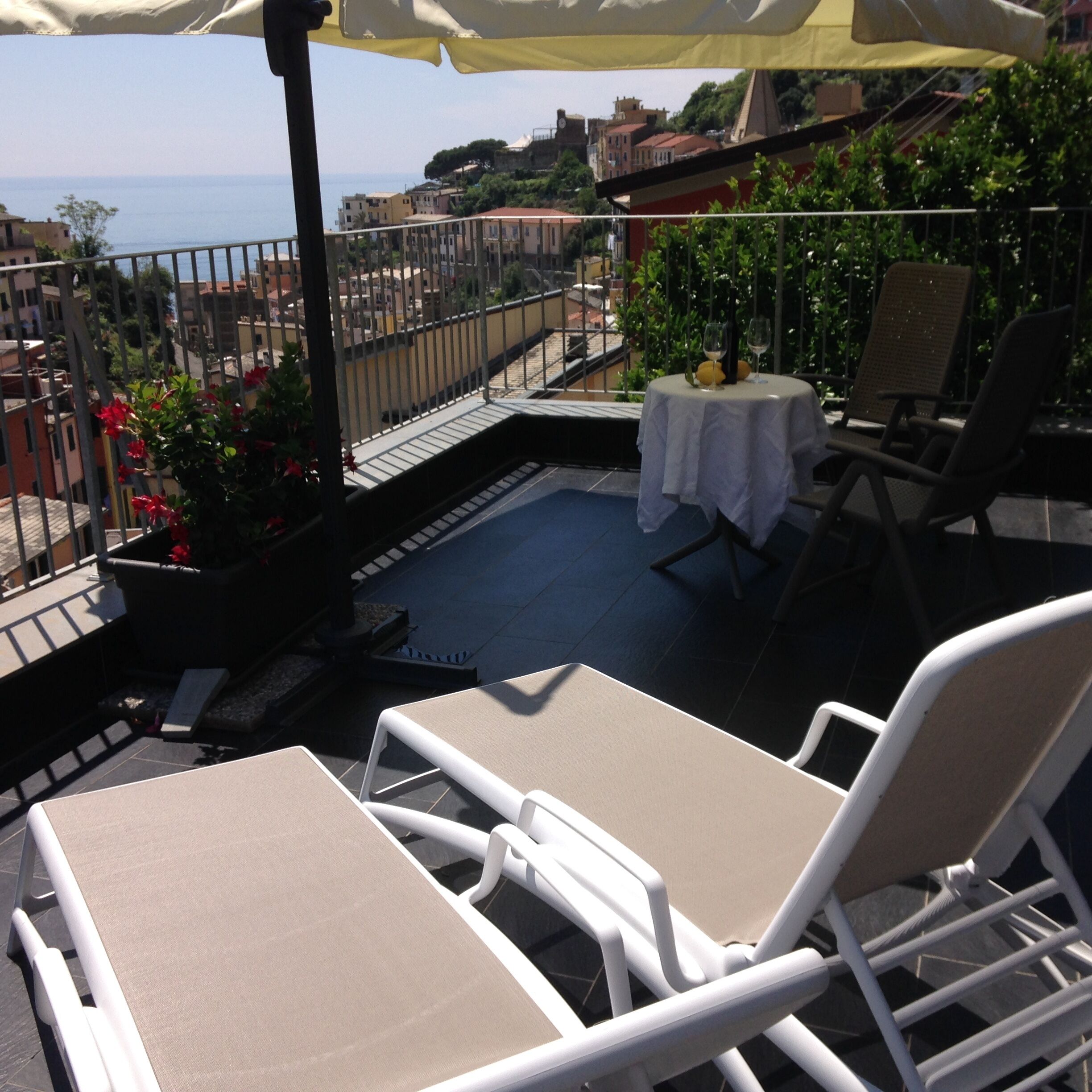 Eine Dachterrasse mit zwei weißen Lounge-Stühlen, einem kleinen Tisch mit weißem Tischtuch und einem Topf mit roten Blüten.