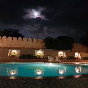 A nighttime pool area with lounge chairs and decorative lighting.