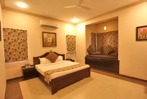 A hotel room with a large bed, a sitting area with a sofa, an air conditioning unit, a ceiling fan, and a framed picture on the wall.