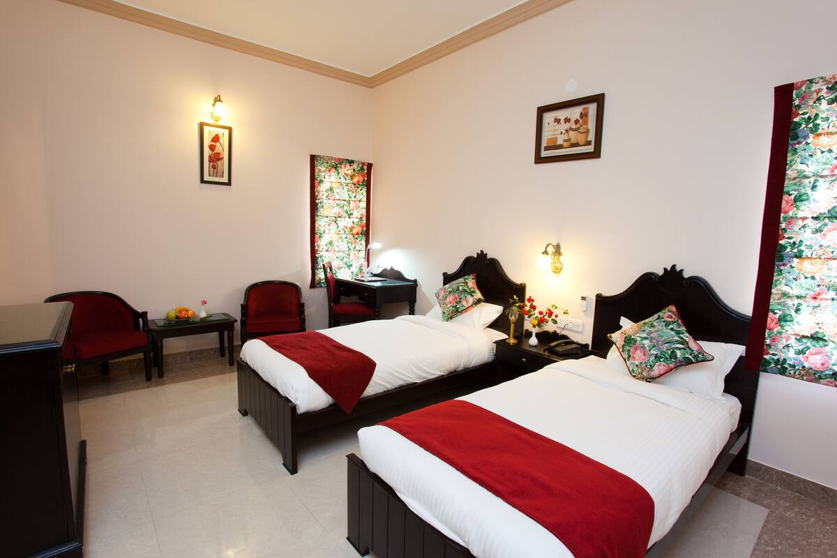 A hotel room with two beds, a desk, a chair, and a small table with a fruit bowl.